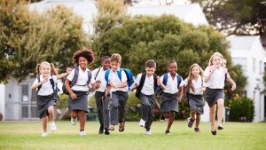 Eight school children in uniform on a field running towards the camera