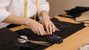 A person with measuring tape around their neck making a school uniform with scissors and black fabric